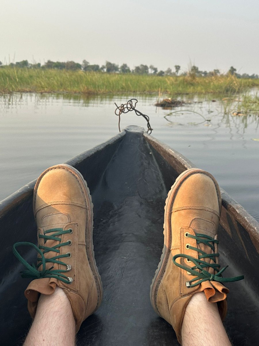 Person wearing Jim Green boots resting their feet on the bow of a mokoro canoe on a river